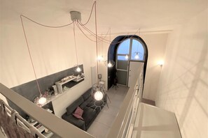 A modern interior with a staircase, a sofa, pendant lights, and a view through an arched window. - LOFT 22 - Moderno a due passi da Piazza del Campo (Siena)