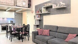 A modern kitchen with a dining area, grey sofa, and decorative shelves. - LOFT 22 - Moderno a due passi da Piazza del Campo (Siena)