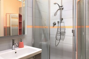 Een moderne badkamer met een douchecabine van glas, een witte wastafel met een roze zeepdispenser en een handdoekrek.