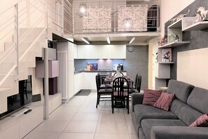 A modern kitchen with a dining area, a grey sofa, and a staircase. - LOFT 22 - Moderno a due passi da Piazza del Campo (Siena)