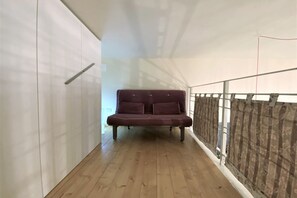 A corridor with a wooden floor, a dark-colored sofa, and a white wall with a door on the left. - LOFT 22 - Moderno a due passi da Piazza del Campo (Siena)