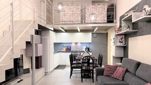 A modern kitchen with a dining area, a grey sofa, and a staircase. - LOFT 22 - Moderno a due passi da Piazza del Campo (Siena)