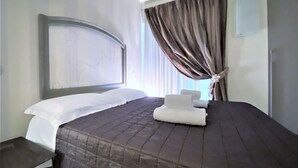 A hotel room with a large bed, a headboard, a bedside table, and a window with curtains. - LOFT 22 - Moderno a due passi da Piazza del Campo (Siena)