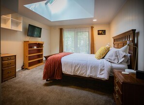 Une chambre à coucher avec un lit, une télévision, une bibliothèque, une fenêtre avec des rideaux et un puits de lumière.