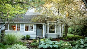A house with a porch, surrounded by lush greenery and a garden. - Briar Rose  (Spokane)