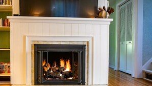 A fireplace with a fire, a bookshelf, and a door in a room with wooden flooring. - Briar Rose  (Spokane)