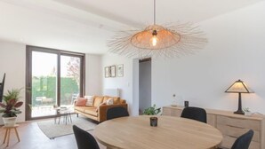 Een moderne eetruimte met een ronde houten tafel, zwarte stoelen en een bijzondere geweven hanglamp.