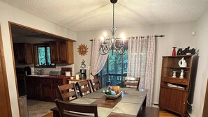 A dining area with a wooden table and chairs, a chandelier, and a view of the kitchen and outdoors. - Cozy Retreat in the Poconos Mountains (Bushkill)