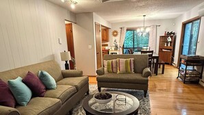 A spacious living room with a wooden floor, a large sofa, a round coffee table, and a dining area in the background. - Cozy Retreat in the Poconos Mountains (Bushkill)