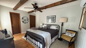 A bedroom with a bed, a bedside table, a lamp, a mirror, and a ceiling fan. - Cozy Retreat in the Poconos Mountains (Bushkill)