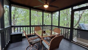 A covered outdoor area with a table and chairs, a ceiling fan, and large windows overlooking a wooded area. - Cozy Retreat in the Poconos Mountains (Bushkill)