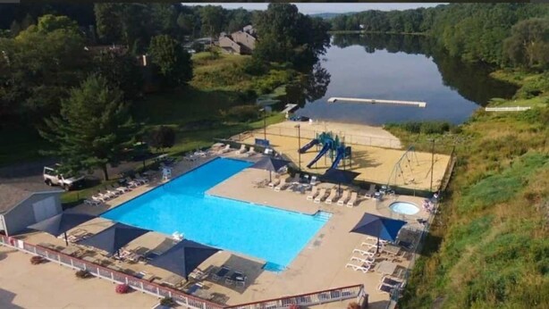 A large outdoor swimming pool with a slide and a separate kiddie pool, surrounded by lounge chairs and umbrellas. - Cozy Retreat in the Poconos Mountains (Bushkill)