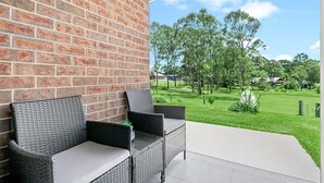 A patio with wicker furniture and a brick wall, overlooking a well-maintained lawn and trees.