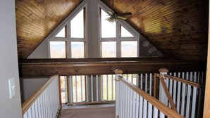 Eine Holztreppe mit weißen Geländern führt zu einem erhöhten Raum mit großen Fenstern.