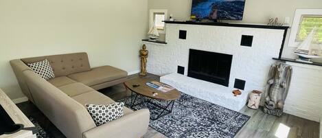 Una sala de estar moderna con un sofá seccional color crema, una chimenea, un televisor de pantalla plana y una alfombra estampada.
