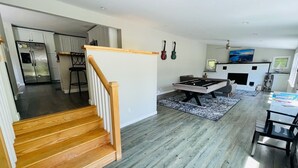 Een moderne keuken met een inbouwkoelkast en fornuis, een eethoek met een pooltafel, en een trap die naar een ander niveau leidt.