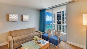 A hotel room with a balcony, a sofa, two armchairs, a coffee table, and artwork on the wall.
