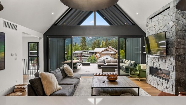 Un salon moderne avec un grand canapé, une table basse et une cheminée. Un téléviseur est fixé au mur et une grande fenêtre offre une vue sur un paysage montagneux.