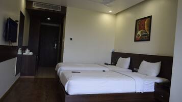 Habitación de hotel con dos camas, un televisor de pantalla plana montado en la pared, un cuadro y un ventilador de techo.