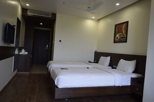 Habitación de hotel con dos camas, un televisor de pantalla plana montado en la pared, un cuadro y un ventilador de techo.
