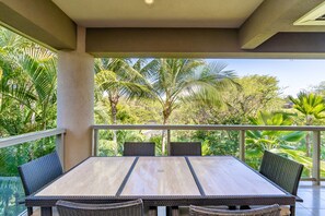 Ein Balkon mit Tisch und Stühlen, umgeben von üppiger Vegetation und Palmen.