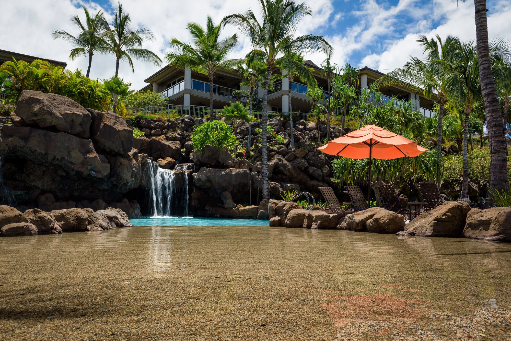 Un resort con piscina cristallina, una cascata e un ombrellone grande.