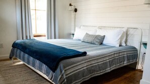 A neatly made bed with a striped bedspread and pillows, a wooden floor, and a window with curtains. - The Cozy Cabernet - short walk to Main St! (Fredericksburg)