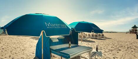 A beach resort with blue umbrellas, lounge chairs, and a clear sky.