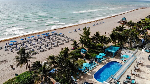 A beach resort with rows of sun loungers and umbrellas, a swimming pool, and a lifeguard tower. - Marenas Ocean View Apartment (Sunny Isles Beach)