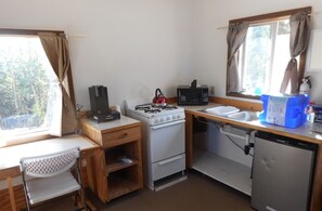 Compact kitchen with a stove, microwave, refrigerator, sink, and desk with a chair.