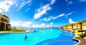 A large outdoor swimming pool with a view of the ocean, surrounded by buildings with red roofs. - Buzios Beach Resort LX (RJ)