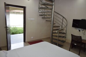 A bedroom with a bed, a TV, a chair, a desk, a red rug, and a spiral staircase.