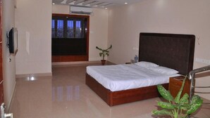 A modern bedroom with a large bed, a ceiling fan, a potted plant, and a view through a window. - Karaikal Ashok Beach Resort (Karaikal)