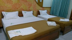 Ett hotellrum med två sängar, båda med vita sängkläder och kuddar, och en brun sänggavel. Det finns ett träbord vid sängen med en hopvikt handduk och en väckarklocka på väggen.