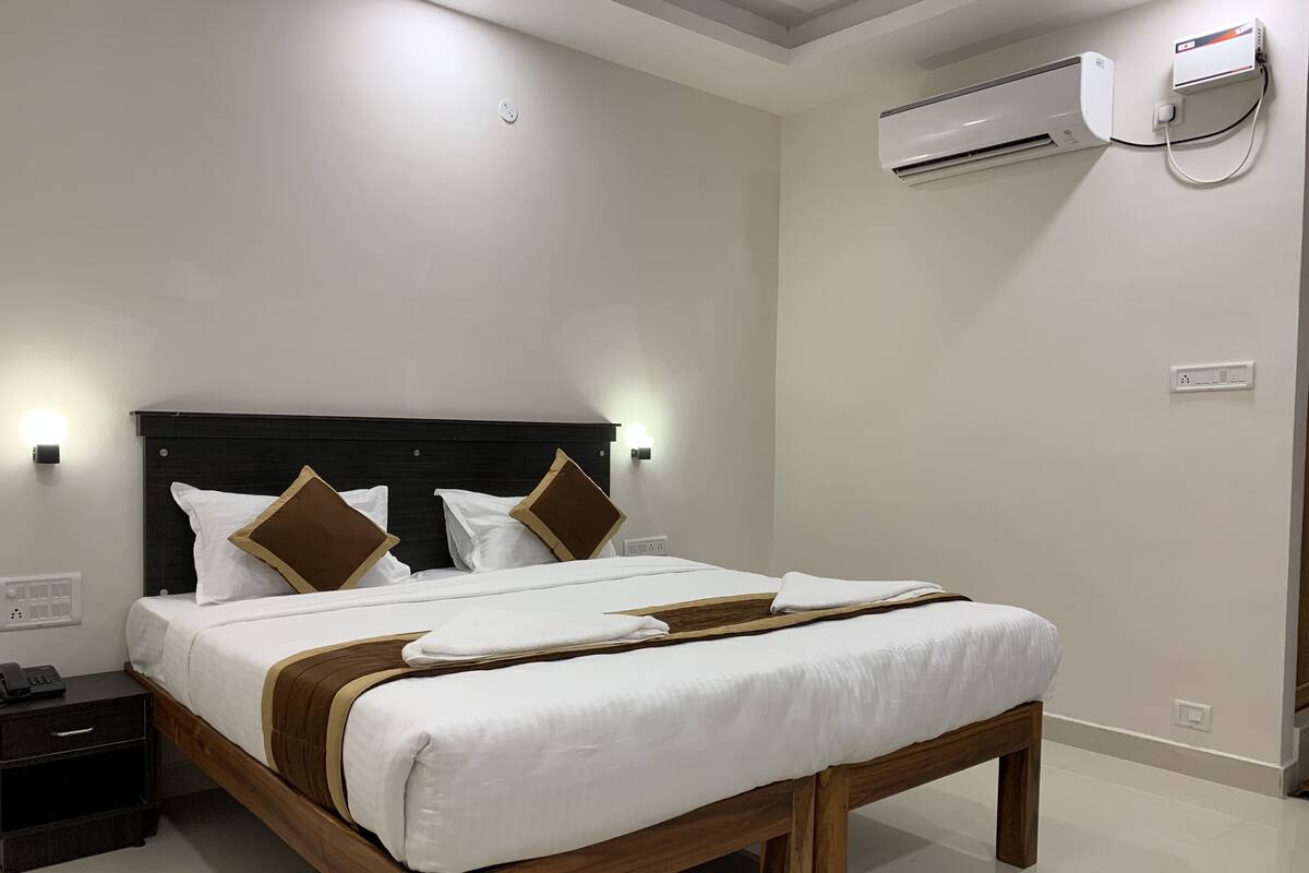 A neatly made bed with a wooden frame and white bedding, a bedside table with a phone, and an air conditioning unit mounted on the wall.
