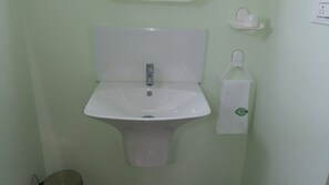 Ett badrum med ett vitt handfat på piedestal, en toalett och en handdukshängare med en handduk på.