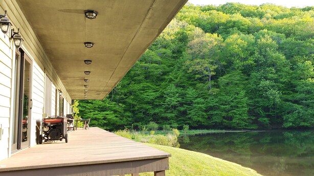Une terrasse en bois équipée d’un barbecue, avec vue sur un lac paisible et une forêt dense.