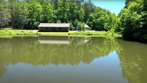 Une maison dotée d’un grand porche, entourée d’un lac et d’une forêt dense.