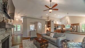 A spacious living room with a fireplace, a large sofa, a coffee table, and a kitchen area in the background.