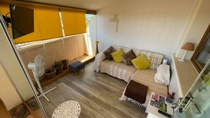 A cozy living room with a sofa, a small table, a fan, and a window with a view. - 2 Bed Penthouse - Sleeps 4 - Pool - Sea Views (Finestrat)