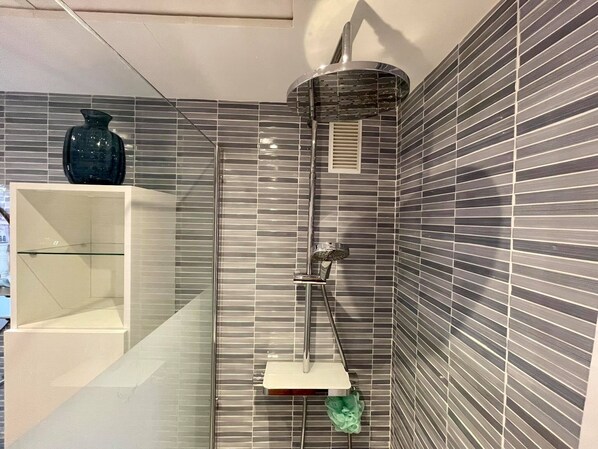 Ducha con mampara de vidrio, cabezal de ducha de mano y panel de control en la pared.