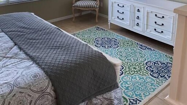 A bedroom with a bed, a television on a dresser, a chair, and a patterned rug.