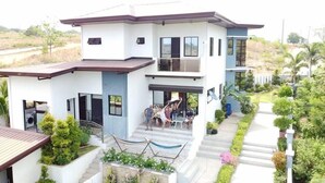 Uma casa moderna de dois andares com varanda, um pequeno jardim e uma rede.