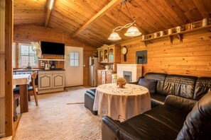 A cozy cabin interior with a dining area, a fireplace, a living room with a leather couch, and wooden walls. - The Small Guest House with Pool, Wi-Fi & Garden (Sudwalde)