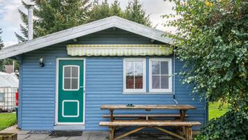 Una cabaña pequeña de color azul con una puerta, ventanas y una mesa de picnic.