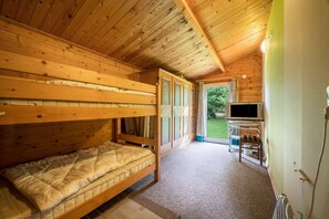 Una habitación tipo cabaña de madera con literas, televisor y vistas al exterior.
