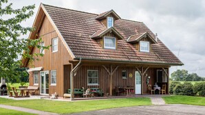 Ein Holzhaus mit geneigtem Dach, einer Veranda mit Sitzgelegenheit und einem sichtbaren Schornstein.