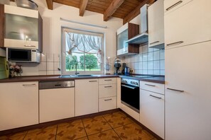 Eine Küche mit weißen Schränken, einem Geschirrspüler, einem Backofen, einer Mikrowelle und einem Fenster mit Blick auf Bäume.
