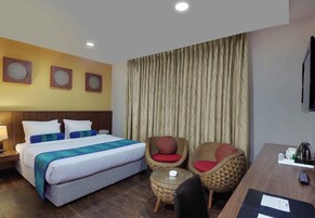 Ein Hotelzimmer mit einem Bett, zwei Korbstühlen, einem kleinen Tisch und einem Schreibtisch mit einer Fernbedienung.