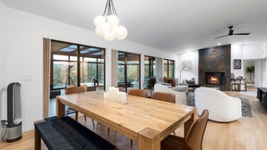 Amplia sala de estar con una gran mesa de comedor de madera, asientos cómodos, chimenea y ventanas amplias que ofrecen vistas al exterior.